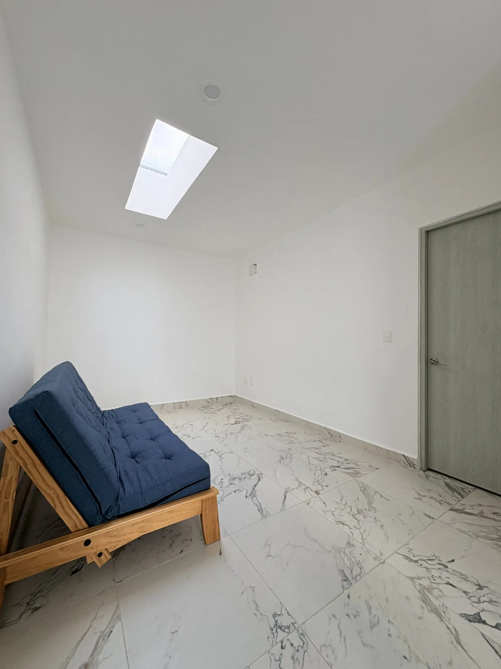 Minimalist room with blue futon and skylight