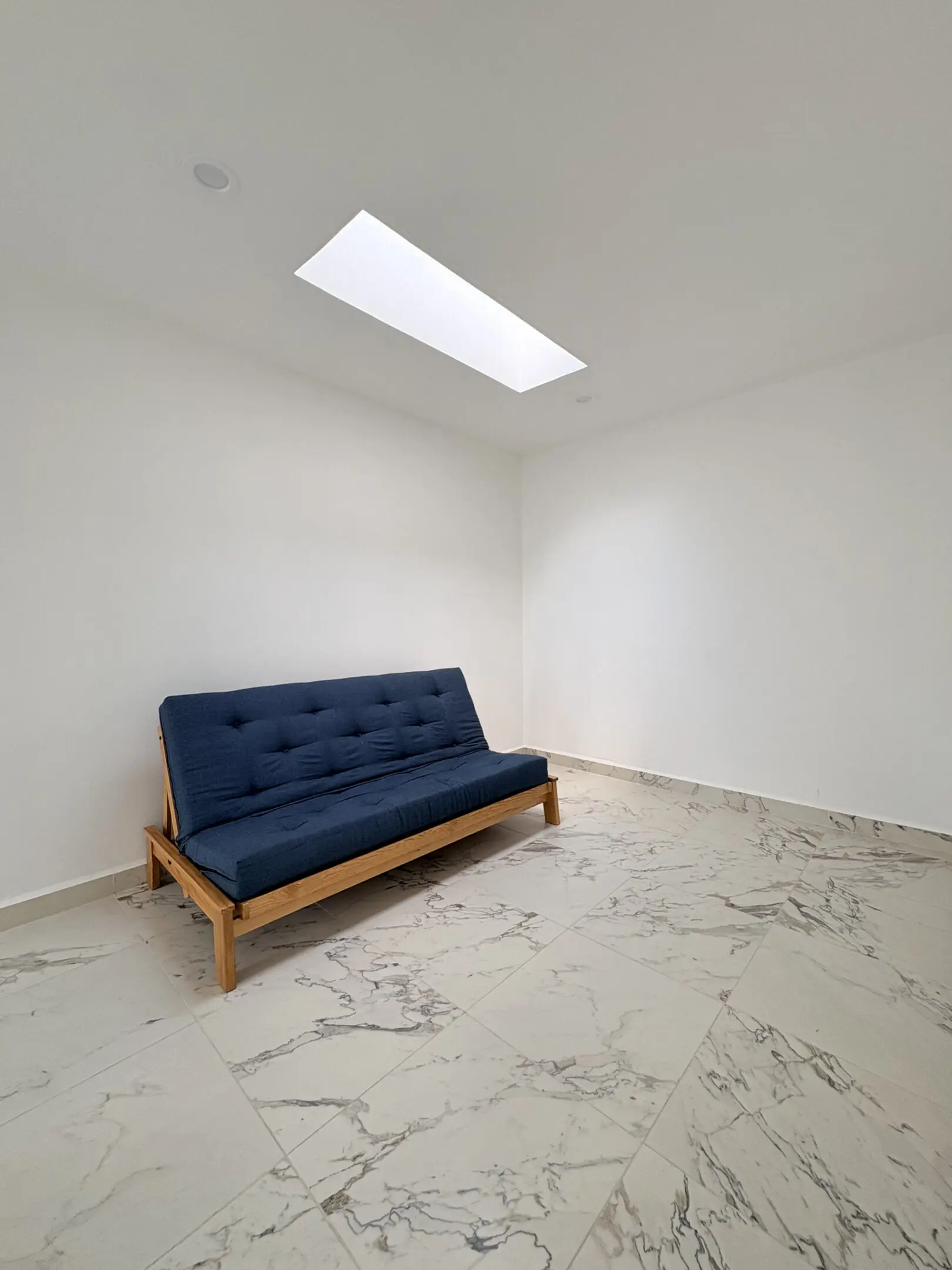Minimal room with navy futon and skylight