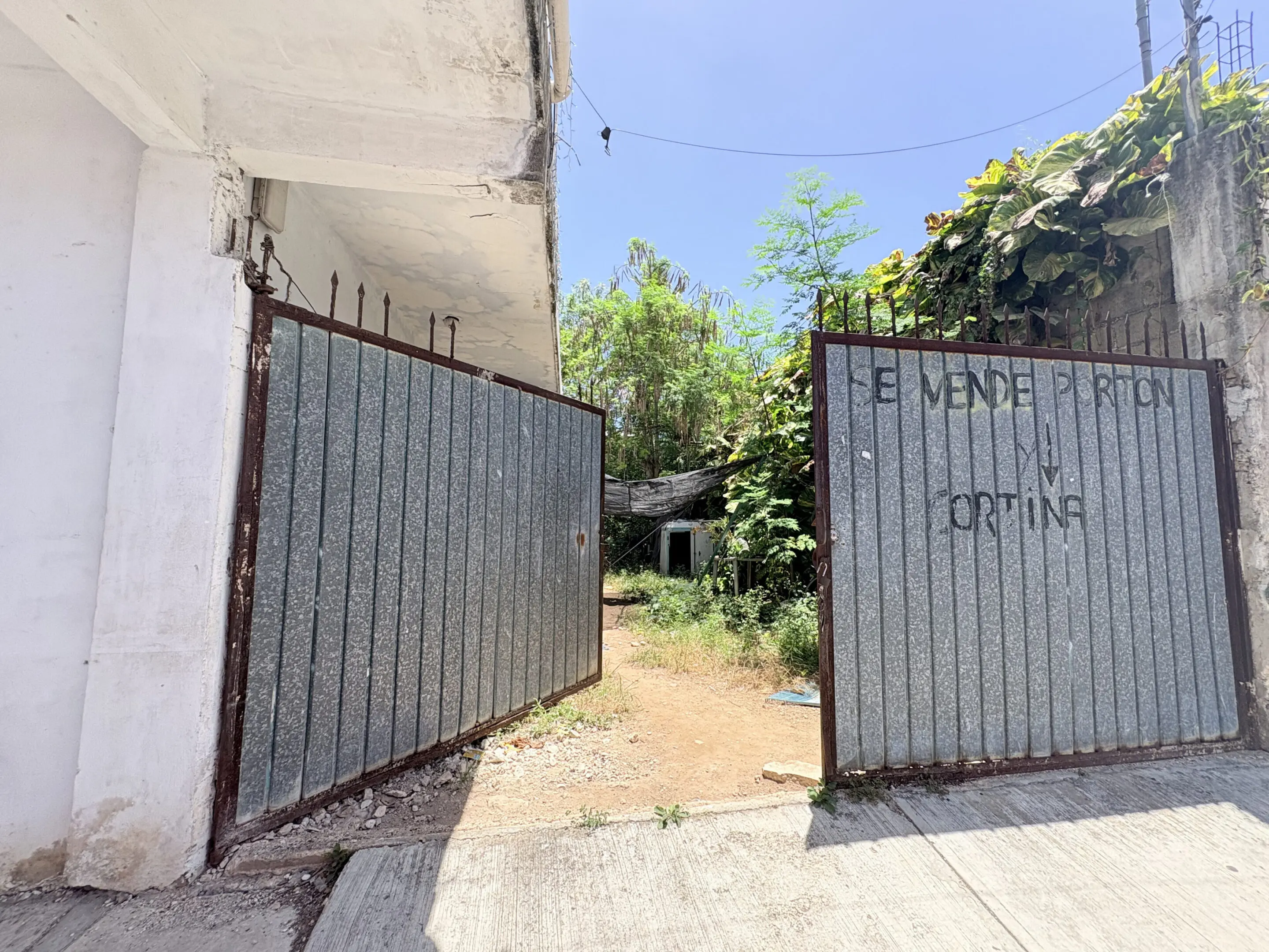 Open corrugated metal gates to overgrown yard