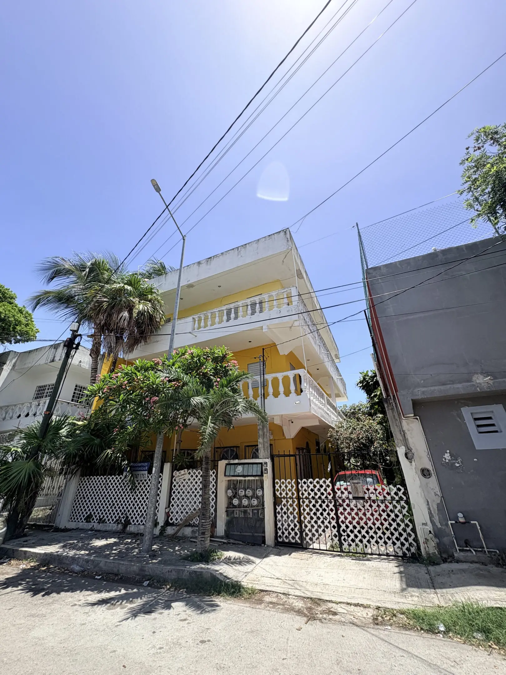 Yellow three-story house with balconies and palms