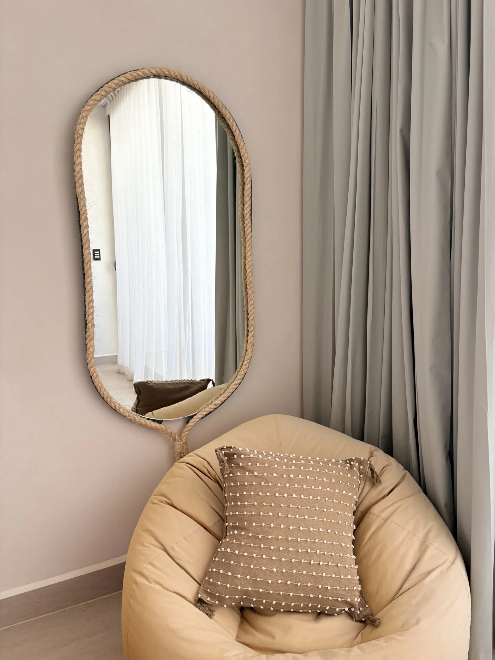 Rope-framed mirror above beige bean bag chair