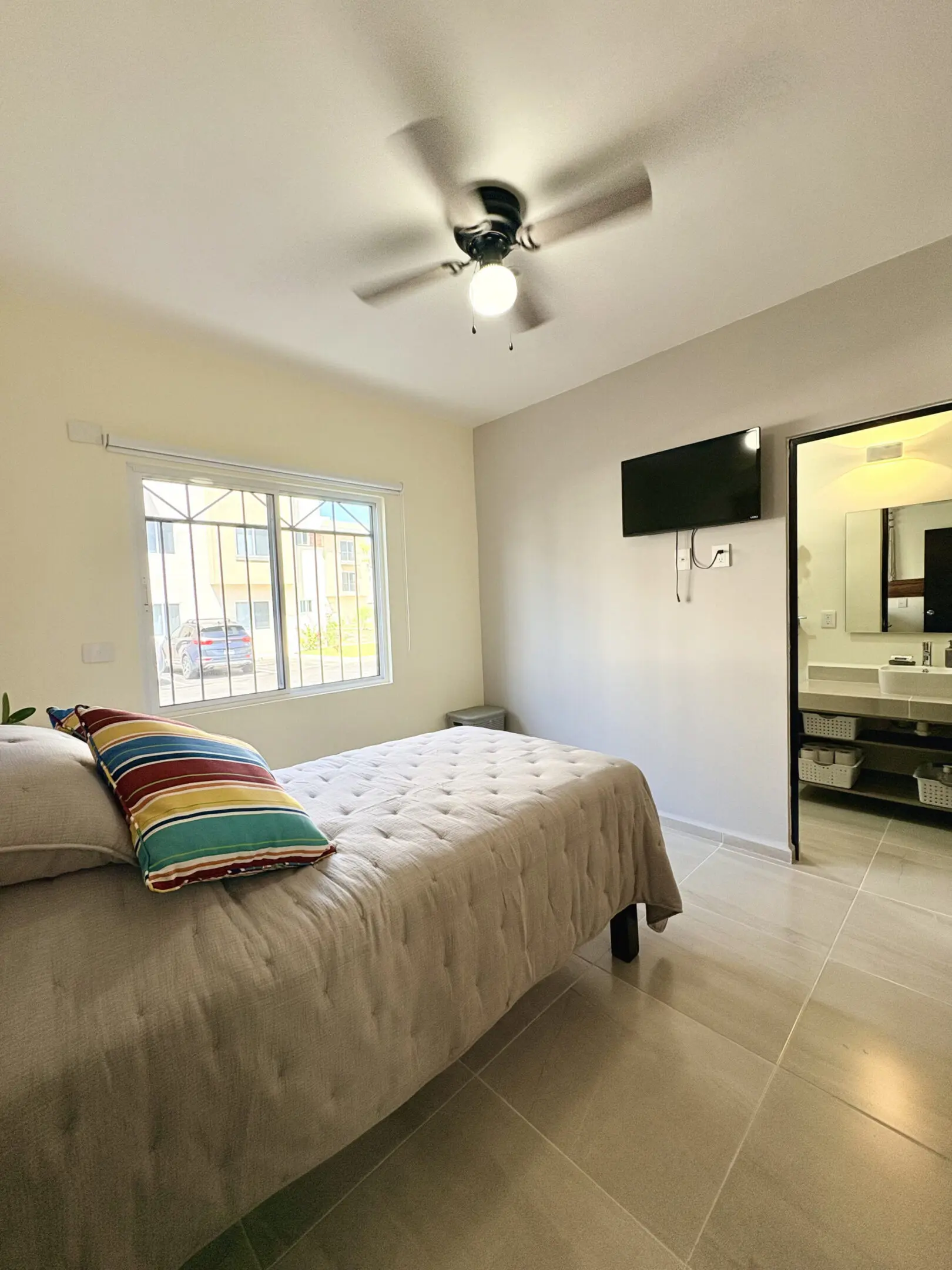 Bright bedroom with bed, colorful pillows, TV